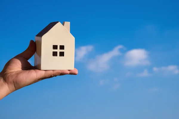 Mano in possesso di un modello di casa e un cielo blu sullo sfondo — Foto Stock