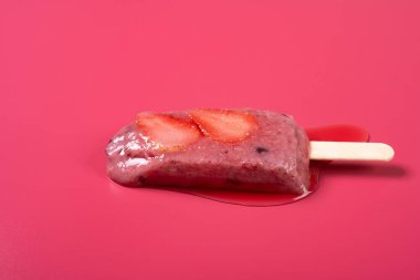 Brezilya böğürtlen aromalı dondurma ve çilek dilimleri kırmızı bir arkaplanda erimeye başlar.