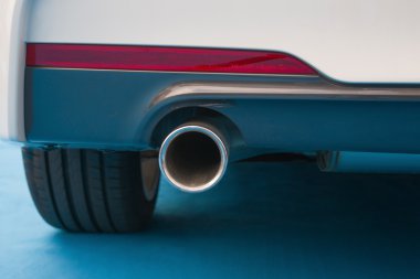 Mavi halı üzerinde beyaz bir otomobilin egzoz borusu