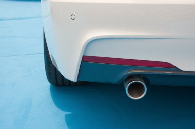 Mavi halı üzerinde beyaz bir otomobilin egzoz borusu