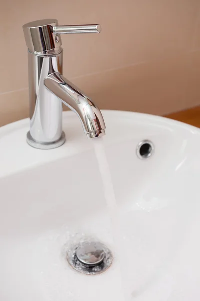 Vatten som rinner från rostfritt stål kran till handfat i badrum — Stockfoto