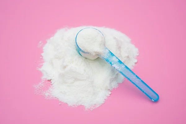 Mleko w proszku w niebieski łyżką na różowym tle, zbliżenie — Zdjęcie stockowe