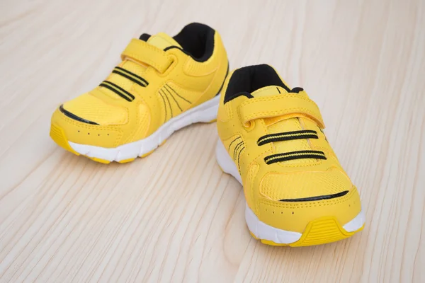 Pair of yellow sporty shoes for kid on a wood background — Stock Photo, Image