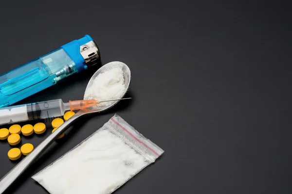 使い捨て注射器と白い粉と錠剤とコピー スペースと黒の背景のライターのパック — ストック写真
