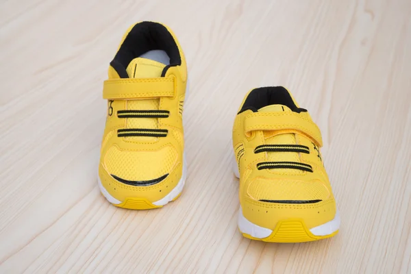 Par de zapatos deportivos amarillos para niños sobre un fondo de madera — Foto de Stock