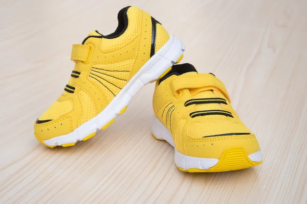 Par de zapatos deportivos amarillos para niños sobre un fondo de madera — Foto de Stock