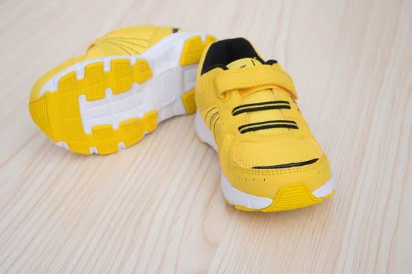 Par de zapatos deportivos amarillos para niños sobre un fondo de madera — Foto de Stock