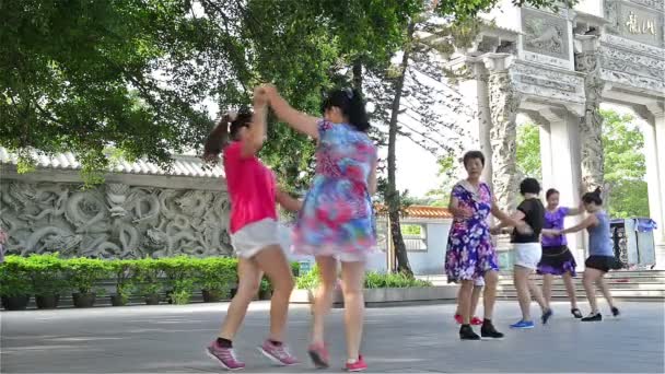 Zhongshan Guangdong Κίνα - 22 Αυγούστου 2015: Μια ομάδα των κινεζικών γυναικών που χορεύουν με τη μουσική μπροστά από ένα πάρκο το πρωί στις 22 Αυγούστου 2015, στο Zhongshan, Guangdong, Κίνα. Τετραγωνικός χορός είναι πολύ δημοφιλής στην — Αρχείο Βίντεο