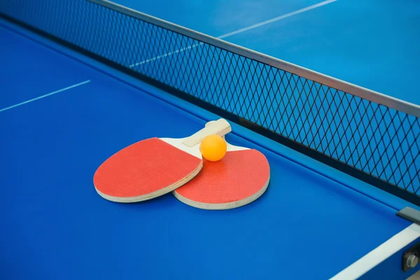 Raquetes de pingpong e bola e rede em uma mesa de pingpong azul — Fotografia de Stock