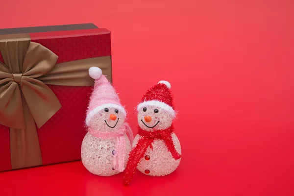 Dwa uśmiechający się zabawka christmas snowman i pudełko na czerwonym tle z kopii przestrzeni — Zdjęcie stockowe