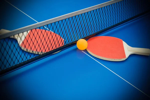 Raquetas de pingpong y pelota resaltadas en una mesa de pingpong azul —  Fotos de Stock