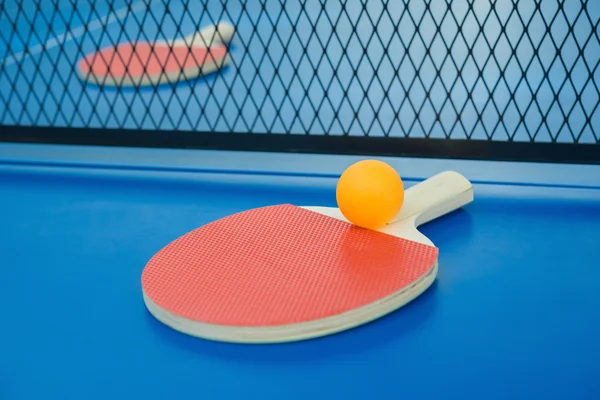 Raquetes de pingpong e bola e rede em uma mesa de pingpong azul — Fotografia de Stock