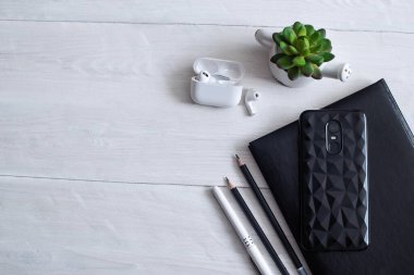 Üzerinde not defteri, kulaklık ve telefon olan beyaz bir masa görüntüsü..