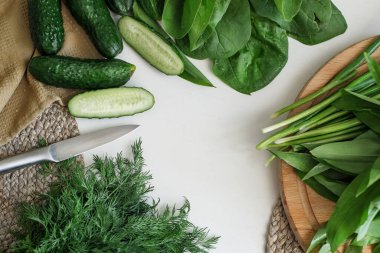 Sliced fresh cucumbers in a bowl, green onions, dill, and on a cutting board. Ingredients for a summer salad on a white tree.