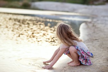 Küçük bir kız eliyle nehre dokunuyor. Yazın gün batımında nehir kenarında bir kız.