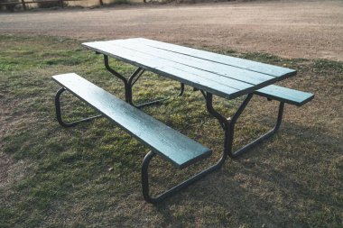 Ahşap piknik masası, toprak bir yolun yakınındaki çimenlik bir arazide.