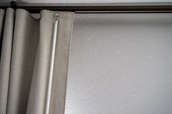 Beige colored curtains with rod close up, against a wall
