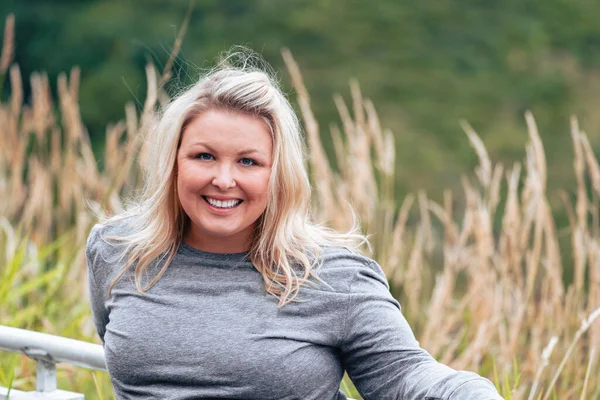 Portrait of a confident young blonde woman, background of grassy reeds