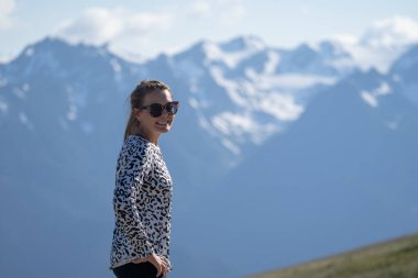 Cute woman stands and poses at Hurricane Ridge, wearing an animal print top