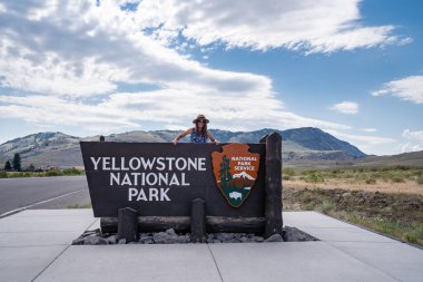 Montana, ABD - 4 Temmuz 2021: Genç bir kadın yaz günü Yellowstone Ulusal Parkı giriş tabelasında poz veriyor