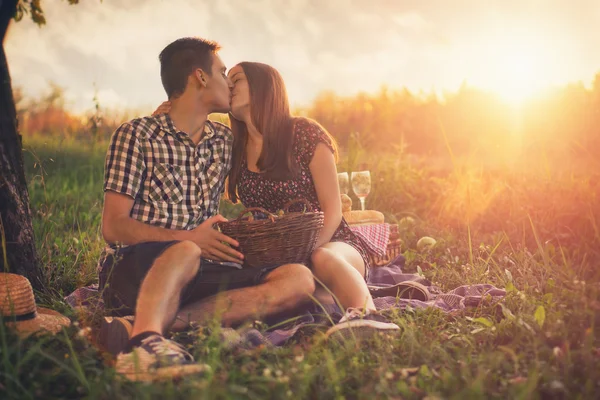 Casal atraente desfrutando de piquenique romântico ao pôr do sol no campo . — Fotografia de Stock