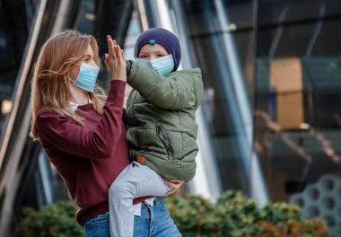 Şehirdeki sokakta maskeli çocukların olduğu bir aile. Anne ve çocuk koronavirüs ve grip salgını sırasında yüz maskesi takıyor. Aile salgın sırasında yürüyüşe çıkmış. Annem oğluna beş tane verir..