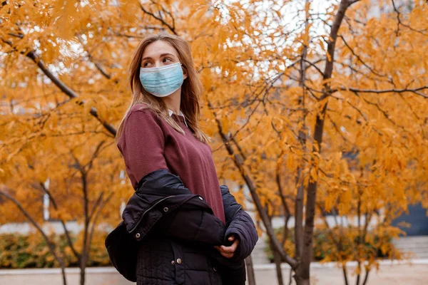Girl in a mask near the business center. Woman in medical mask outdoors in autumn. Epidemic in the fall. Female student during the epidemic. Protection against COVID-19.