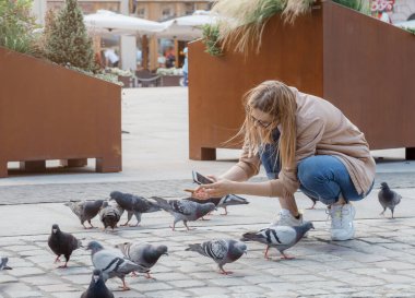 Kuşların yanında güzel bir kadın. Şehirde güvercinler var. Kız şehirdeki meydanda güvercinleri dağıtıyor. Seyahat.