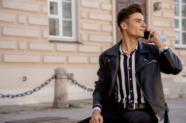 Sokakta oturan şık bir adam. Cep telefonu olan genç bir adam. Adam telefonu kullanıyor. Adam ve alet..