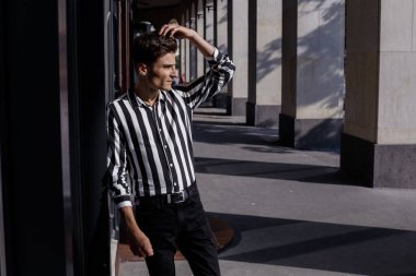 Moda tarzı olan kendine güvenen genç bir adam. Sokak modası konsepti. Kapatın. Siyah kot giyen şık bir adam Avrupa 'daki eski bir binaya karşı basamaklarda duruyor..