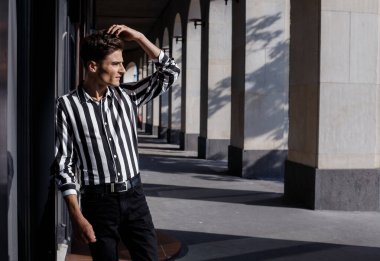 Moda tarzı olan kendine güvenen genç bir adam. Sokak modası konsepti. Kapatın. Siyah kot giyen şık bir adam Avrupa 'daki eski bir binaya karşı basamaklarda duruyor..