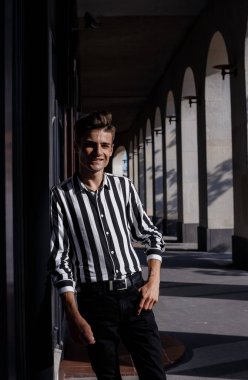 Moda tarzı olan kendine güvenen genç bir adam. Sokak modası konsepti. Kapatın. Siyah kot giyen şık bir adam Avrupa 'daki eski bir binaya karşı basamaklarda duruyor..