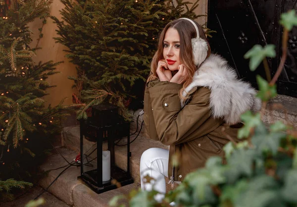Dame en pull tricoté et écouteurs moelleux. Portrait extérieur de jeune belle fille souriante heureuse porte manteau de fourrure près décoré arbre de Noël. — Photo