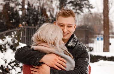Nazik bir kucaklaşmada sevgi dolu bir çift. Adam kız arkadaşını öpüyor. Sevgililer Günü. Genç adam kış parkında kız arkadaşına sarılıyor..
