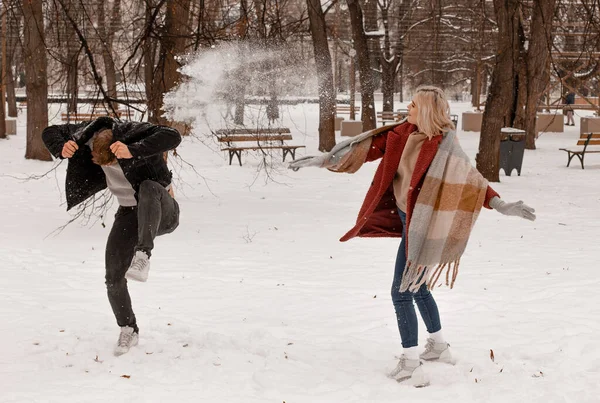 Couple playing with snow and girlfriend throwing a ball in winter holidays. Happy young interracial couple playing together in the snow. Outdoors while falling snow.