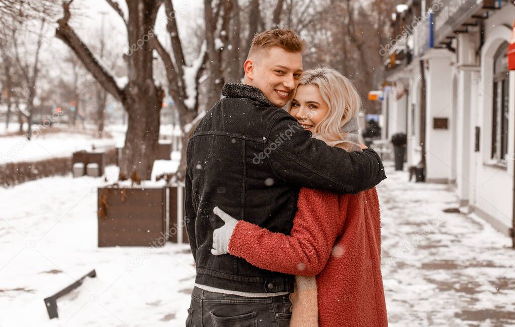 Outdoor waist up portrait of young beautiful happy smiling couple posing on street. Copy, empty space. Embracing dates in winterwear looking at camera in natural environment. Winter Vacation.