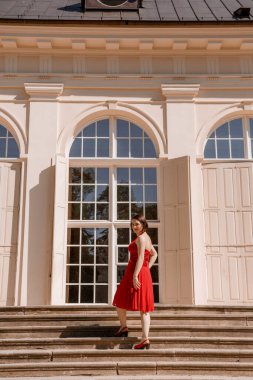 Büyük Portakal Varşova 'daki Lazienki Krolewskie parkında klasik bir portakaldır. Bahçedeki Kadın, Çiçeklerdeki Yaşlı Beyaz Koyak, Açık Hava Güzellik Portresi. Kırmızı elbiseli bir kadın oturuyor. Polonya.