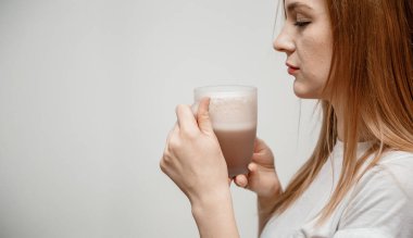 Kadın eli sıcak içki bardağını tutuyor. O gülümsüyor ve kahve aromasını içine çekmek için elinde bir fincan kahve tutuyor. Cappuccinolu güzel, mutlu bir kadın..