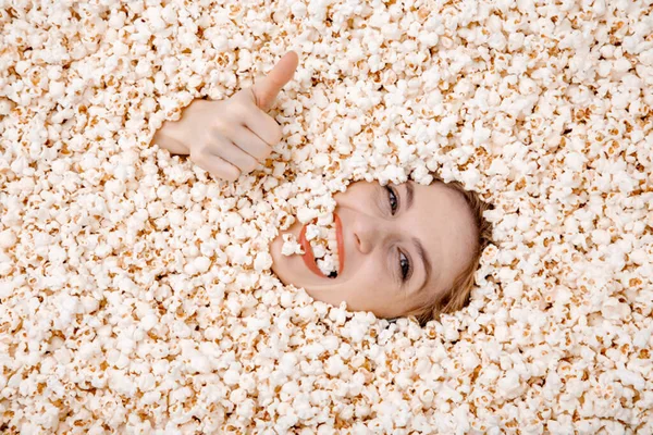 Ritratto femminile in popcorn. Immagine di una bella donna europea sulla ventina che mangia popcorn. Mangiare popcorn. Giovane donna sepolta nei popcorn. graziosa femmina modello sepolto in popcorn con solo il suo faccia mostrando. — Foto Stock