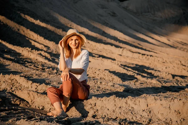 Young beautiful lonely woman with long hair in with straw hat. A lonely girl goes down the sand dunes. Summer fashion poartrait outdoor.