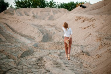 Genç bir kadın şapkasıyla kumlu sahili keşfediyor. Hippi kız, doğa çölünde genç bir gezgin. Bir kadın çölde buluşmak için yürür. Kadın yürüyor.