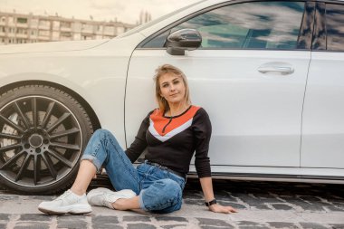 Genç çekici model arabanın yanında oturuyor. Arabanın yanında oturan kız..