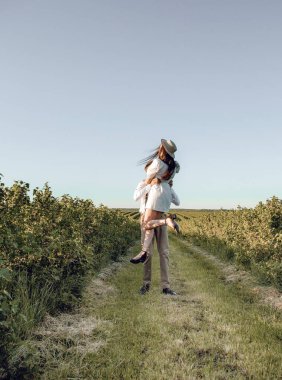 Hipster boho tarzı bağımsız kıyafetler giyen, kırsalda aşık genç bir çift, erkek kadını elinde tutuyor. Çiftler dışarıda eğleniyor..