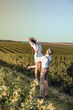 Hipster boho tarzı bağımsız kıyafetler giyen, kırsalda aşık genç bir çift, erkek kadını elinde tutuyor. Çiftler dışarıda eğleniyor..