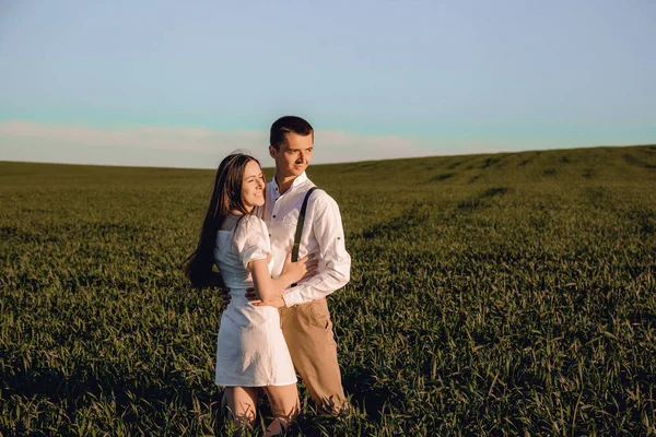 Hermosa pareja enamorada sentada y abrazada en un campo verde con arbustos. Caminando en el campo verde en un día soleado de verano. La naturaleza en el campo. Niño y niña en sombreros. — Foto de Stock