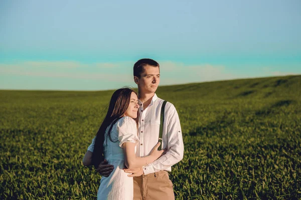 Belo casal apaixonado sentado e abraçando em um campo verde com arbustos. Caminhando no campo verde em um dia ensolarado de verão. Natureza no campo. Menino e menina de chapéus. — Fotografia de Stock