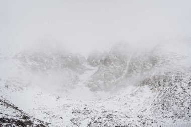 Slovakya 'da kışın sisli ve karlı dağ manzarası. Lomnica yakınlarındaki High Tatras 'ta kayalık tepeler kısmen bulutlarla gizlenmiş dramatik alp manzarası. Kopyalama alanı ve soğuk hava atmosferiyle minimalist doğal arkaplan.