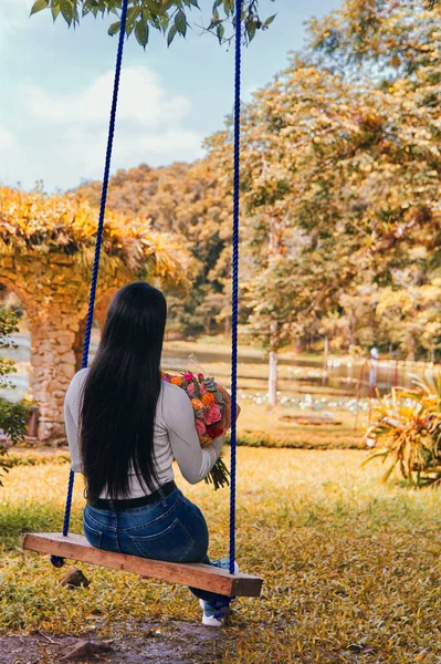 Elinde bir buket çiçekle salıncakta oturan bir kadın.