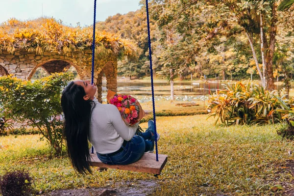 Elinde bir buket çiçekle salıncakta oturan bir kadın.