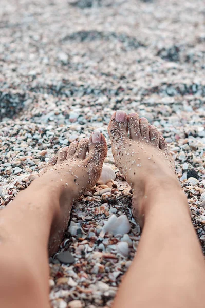 一个女人的脚躺在布满贝壳的海滩上 — 图库照片